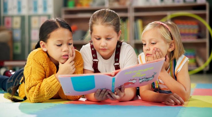 Three students lie on their stomachs reading a book. 
